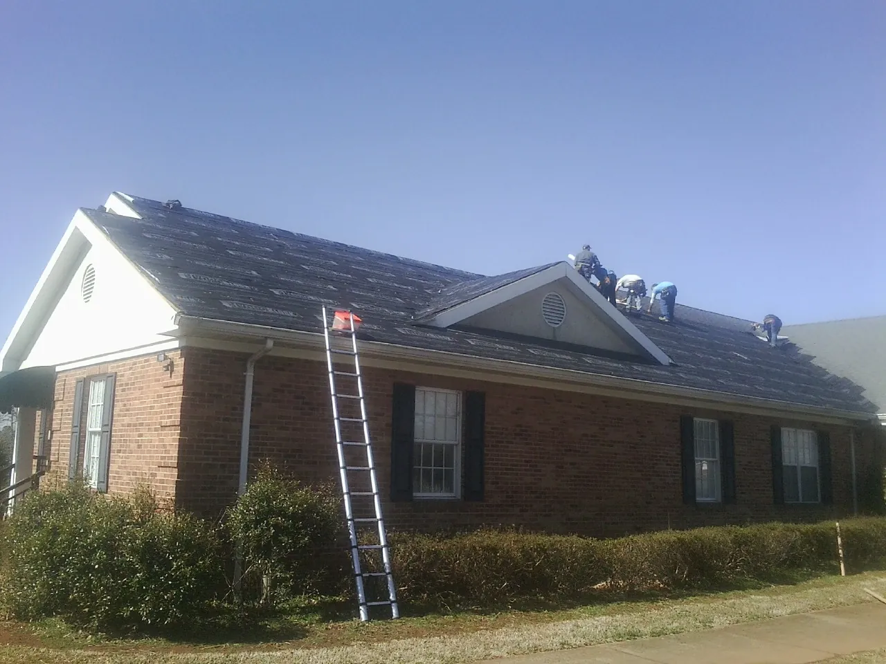 Crew tearing shingles off a brick ranch roof with a ladder set — Metal Roof Repair work by our crew in Clarkston