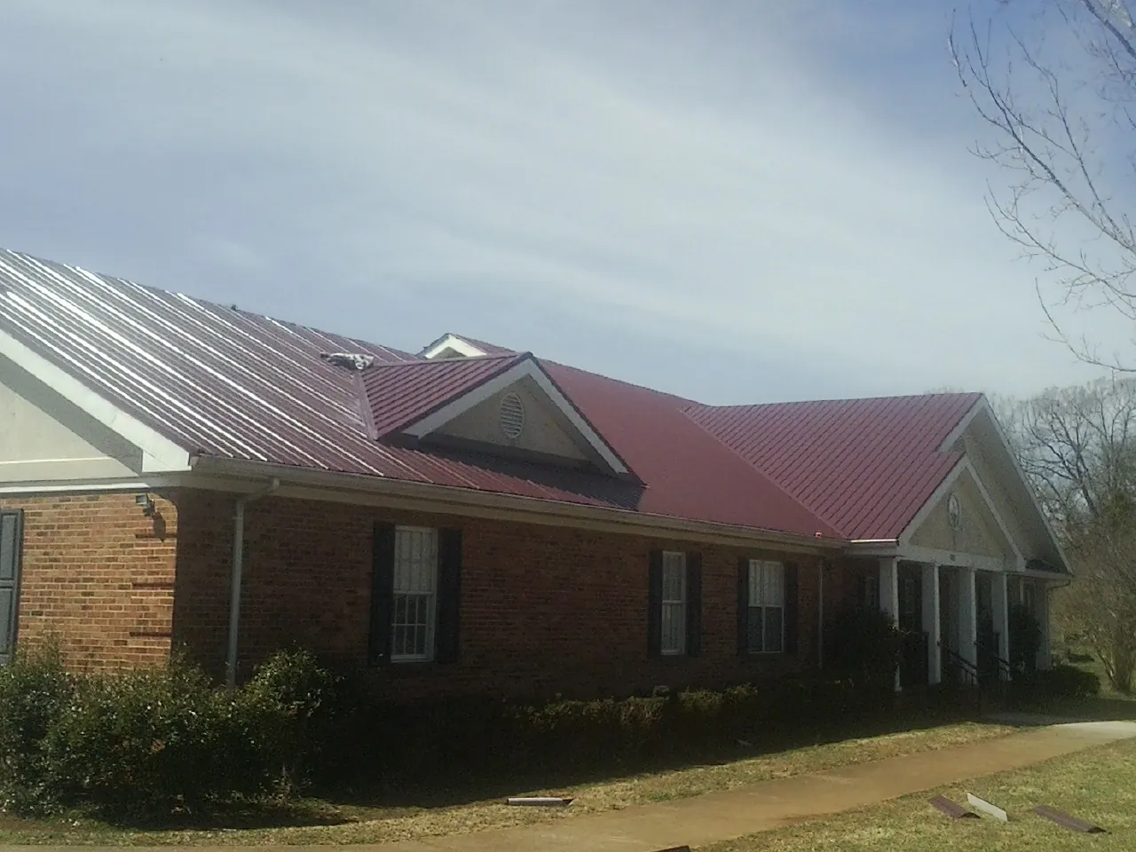 Red metal roof with gabled entries on a long brick building, from a Hail Damage Roof Repair job in Clarkston