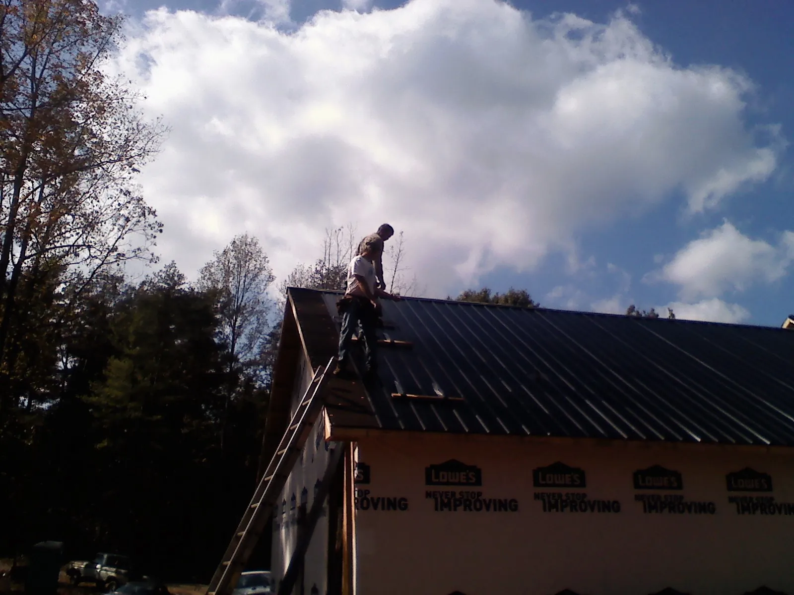 Roofer fastening dark metal panels high against a cloudy sky, from a Roof Inspection job in Clarkston