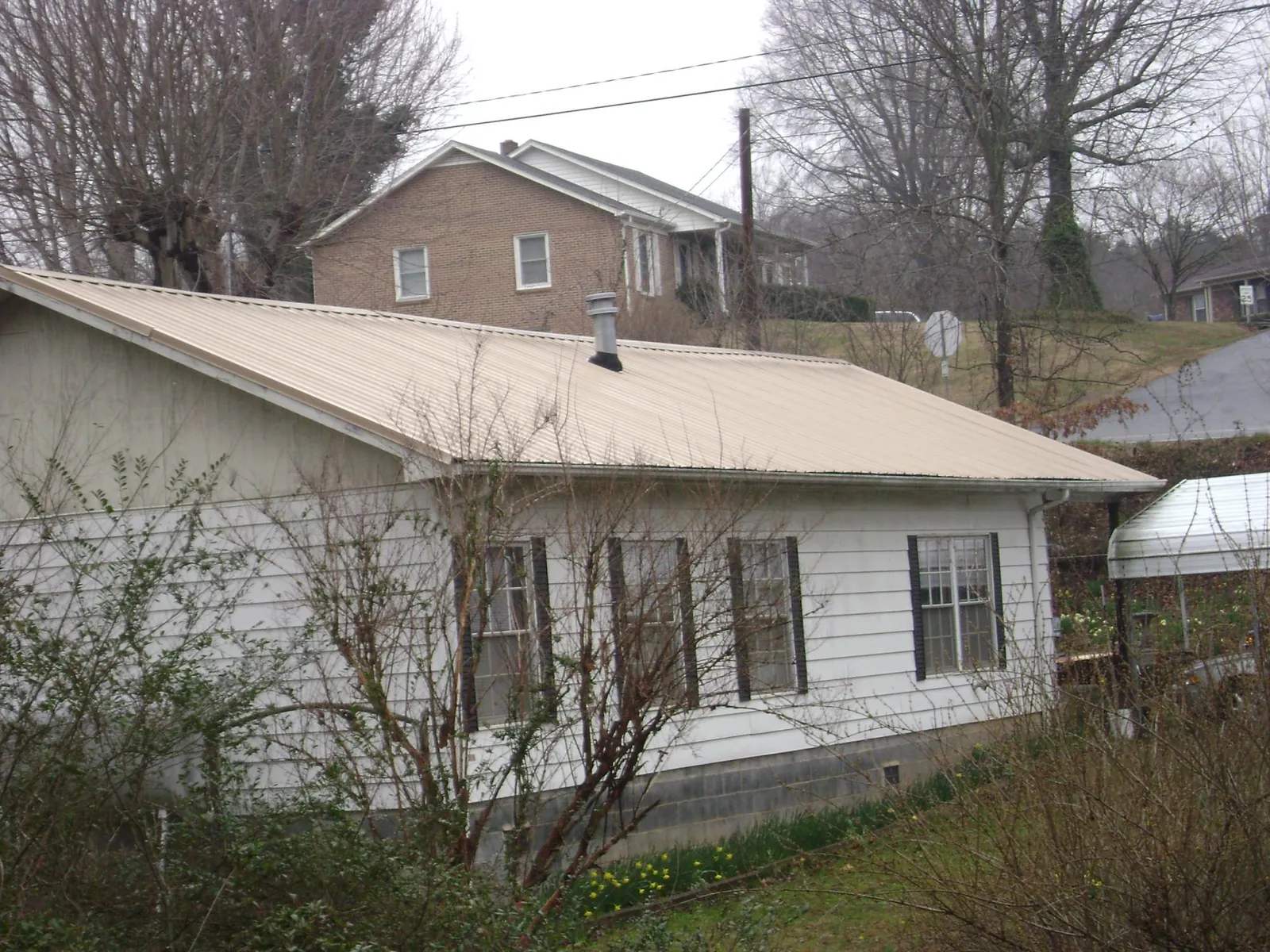 Tan metal roof on a white sided house set into a hillside — Commercial Roofing by Roofing Brothers in Clarkston